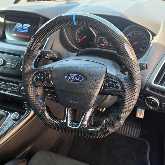 A carbon fiber wrapped steering wheel with blue accents on a Ford RS car interior, showing the dashboard, instrument cluster, and gear shifter.